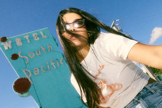 Woman in sunglasses posing in front of the retro South Pacific Motel sign on Biscayne Blvd, captured in lifestyle and street photography style by Mauricio Candela