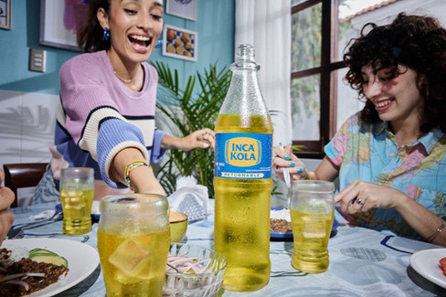 Friends laughing and enjoying a home-cooked meal with chilled Inca Kola