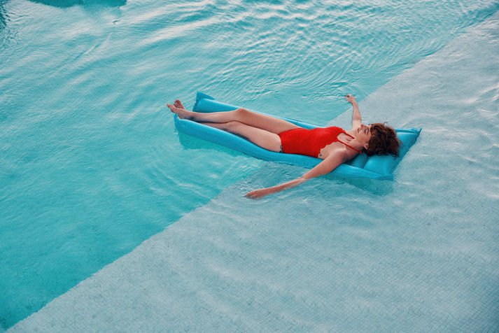 A woman in a red swimsuit leisurely floats on her back in a clear blue pool. 