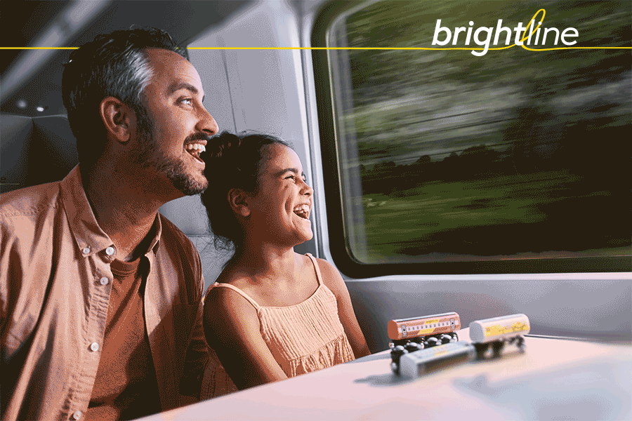 Father and daughter smile while looking out a moving train window. Toy trains are on the table. Brightline logo is at the top.