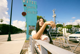 Woman leaning on a railing in front of the vintage South Pacific Motel sign on Biscayne Blvd, photographed in lifestyle and street photography style by Mauricio Candela