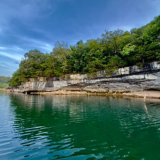 Turquoise Beaver Lake water beside a wooded limestone bluff