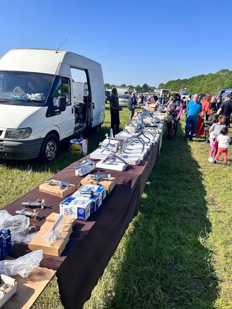 Outdoor car boot sale stall selling chrome bathroom taps and faucets beside a white van with shoppers