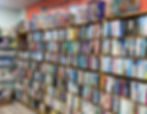Large wall of second-hand books displayed in a charity shop, with shelves filled with fiction and non-fiction titles and jigsaw puzzles on top.