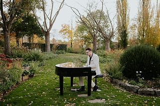 Werbebild für das Adventskonzert von Tom Mayer im DER SALON in Kempten. Der Pianist sitzt an einem Flügel in einem herbstlichen Garten. Das Konzert findet am 10. Dezember 2026 statt.