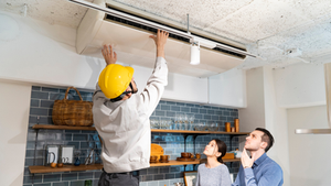 A worker adjusts a ceiling AC unit, illustrating the hidden cost of fixed ownership and certainty