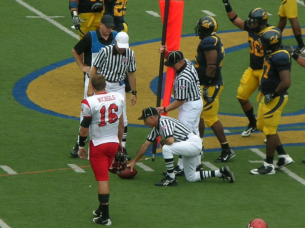 Officials crouch beside the chains to measure whether a fourth-down football reached the first-down marker during a college game.