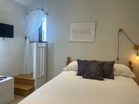 Bedroom with a king size bed in it. White bedding and three purple cushions.  Arched window on the left.
