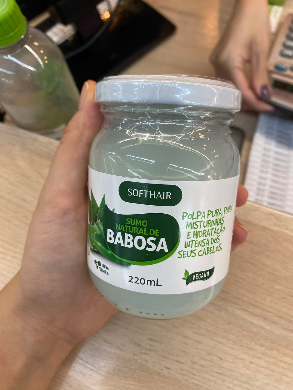Frasco de gel capilar SOFTHAIR Babosa 220 mL na mão, com rótulo verde, em balcão de loja.