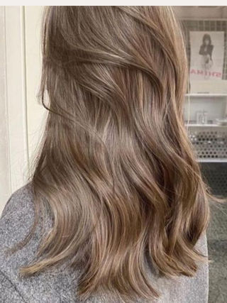Cabelo castanho claro ondulado visto de trás, em salão, com suéter cinza e pôster ao fundo.