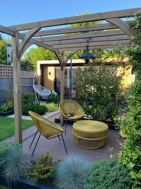 Wooden pergola with yellow acapulco furniture with cedar cladded garden room behind. 