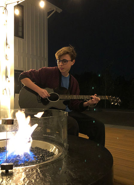 LIAM hopkins playing acoustic guitar by the campfire.