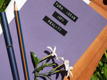 Notebook with “Turn ideas into reality” on the cover, surrounded by pencils and flowers on grass, symbolising creative agricultural copywriting.