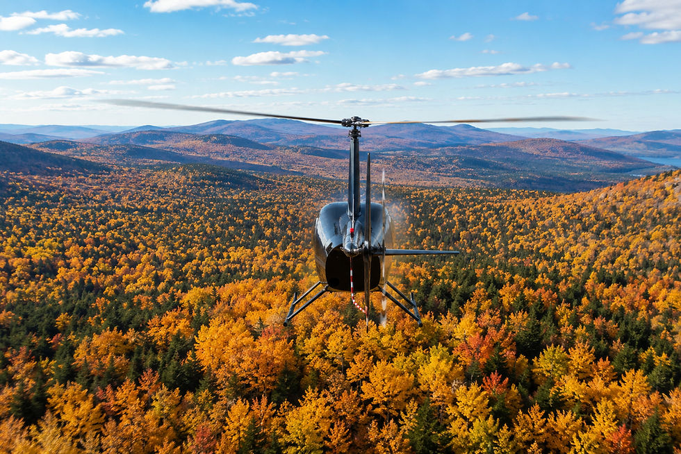 Hélicoptère noir en vol au-dessus des Appalaches, une forêt automnale flamboyante et de montagnes sous un ciel bleu.