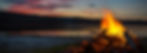 Campfire by a serene lake in California at sunset, with vibrant orange flames, silhouetted trees, and a colorful sky reflecting on the water. Calm mood.