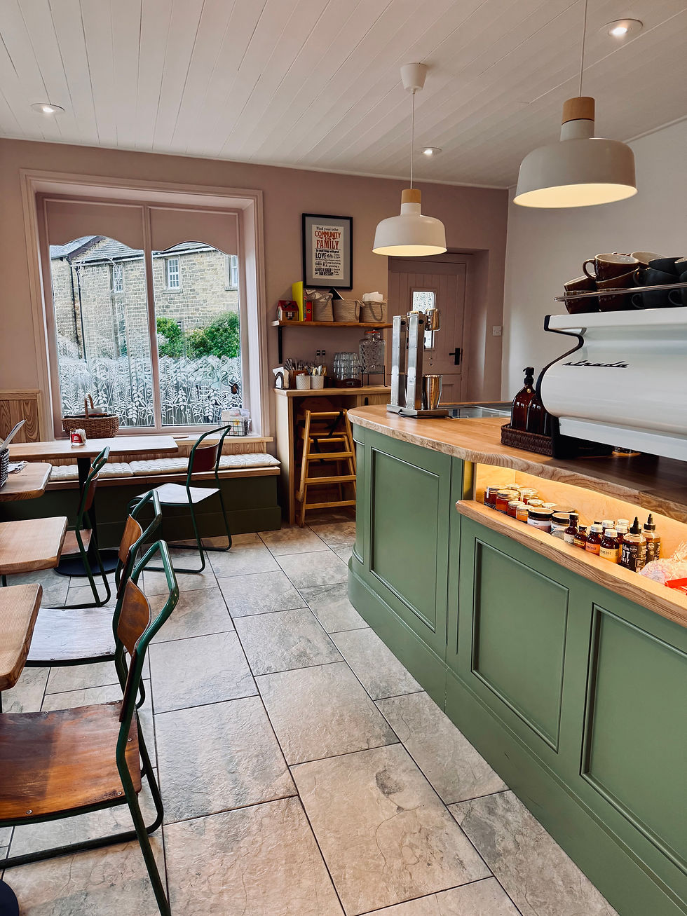 Cozy cafe with green counter, wooden chairs, and wall shelves. Large window overlooks a garden. Pendant lights and warm, inviting decor.