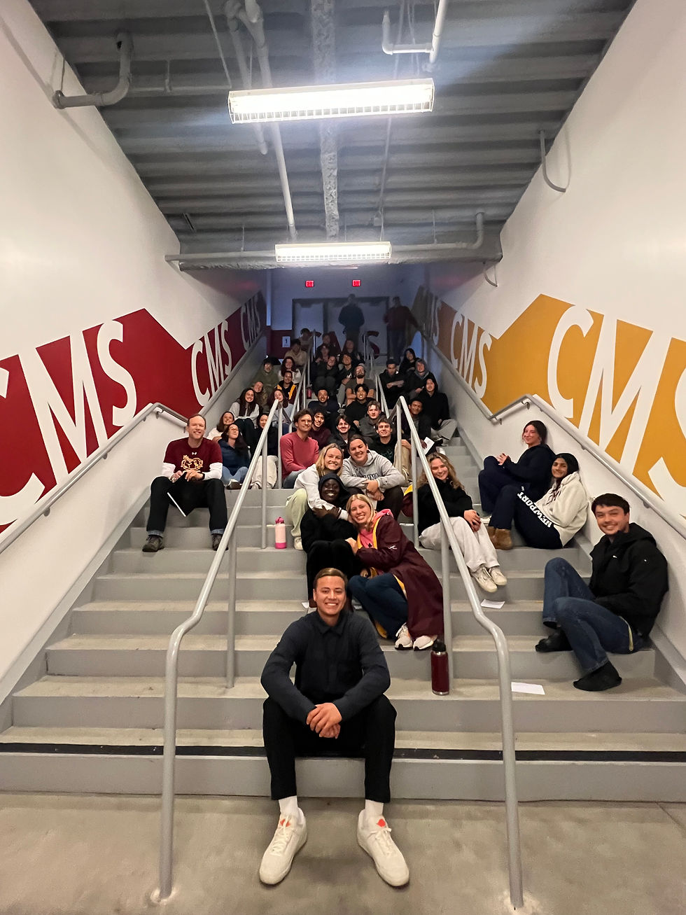 portrait photo of a large group of students sitting on indoor stairs with CMS branding