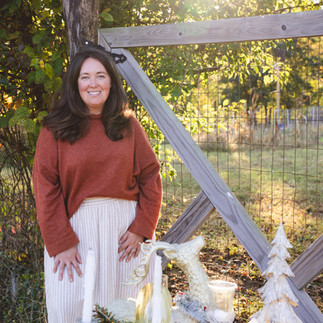 A woman wearing a brown sweater smiling standing near a garden gate