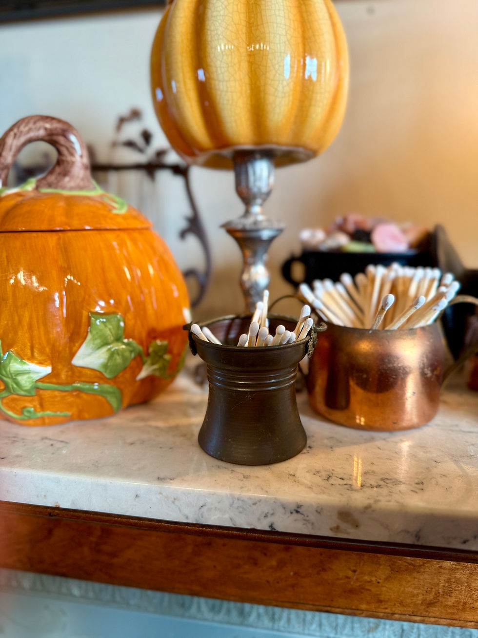 Metal containers hold matches. A candle made in a pumpkin vessel sits on a candle stick holder surrounded by other various pumpkin vessel candles