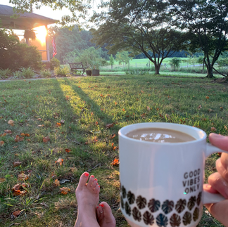 A person sitting in a grassy area with coffee as the sun comes up