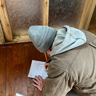 A man in a winter hat and jacket drawing plans inside a trailer