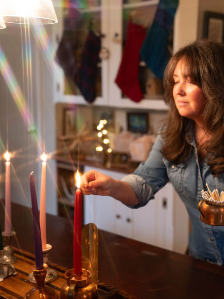 A woman lights a red candle with a match. in the background there are stockings, lights and other Christmas decorations.