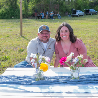 A man and a woman sitting at a picnic table in a field