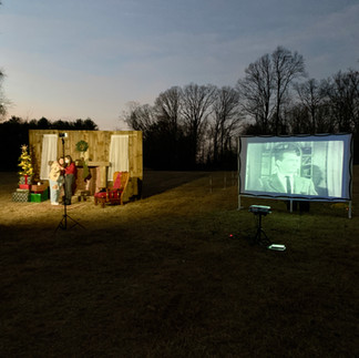 An outdoor movie showing a black and white image on the screen where a family takes a photo at a photo op