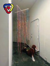 Person laying under an art installation of string and beads. 