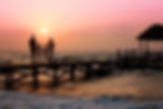 A family walking along a wooden bridge in the sea while the sun is setting