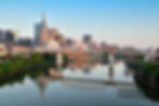 Nashville skyline with modern skyscrapers and a bridge reflecting in a calm Cumberland River. The setting sun casts a warm glow, creating a serene mood.
