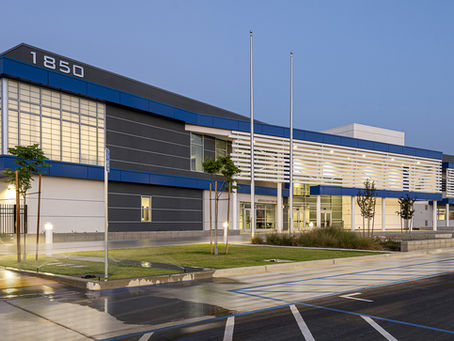 Sanger High School at dusk with blue accents and glass windows. Illuminated streetlights, parking spaces, and trees in the foreground.