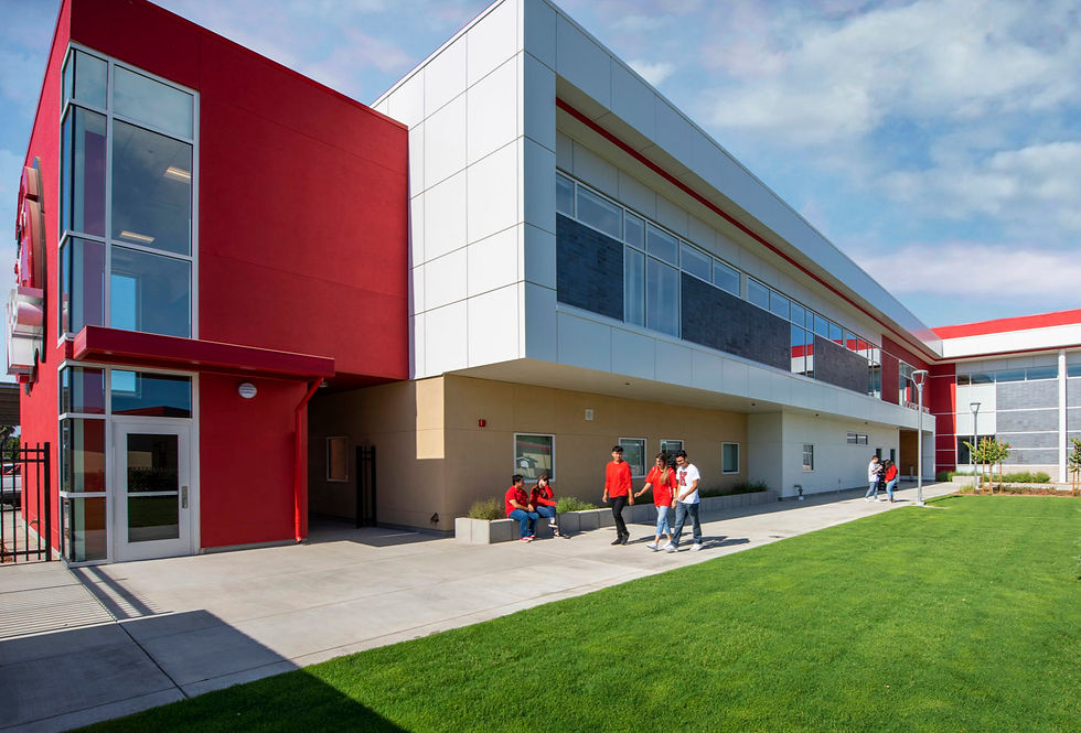 People in red shirts walking and sitting outside a modern building with red and white walls, on a sunny day with green grass lawn.
