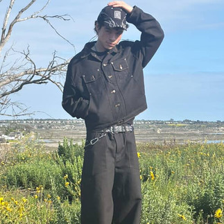 A man with one hand it pocket and the other on head, wearing all black