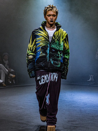Man wearing emo-makeup, colorful hoodie, and dark pants on fashion runway