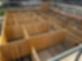 Elevated view of a house under construction with unfinished plywood walls and room framing on a concrete slab.