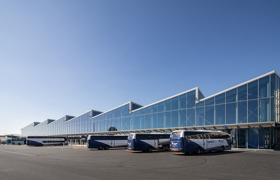 Modern bus terminal with blue glass facade, parked blue and white buses marked "Xpress," clear sky, and an empty asphalt lot.