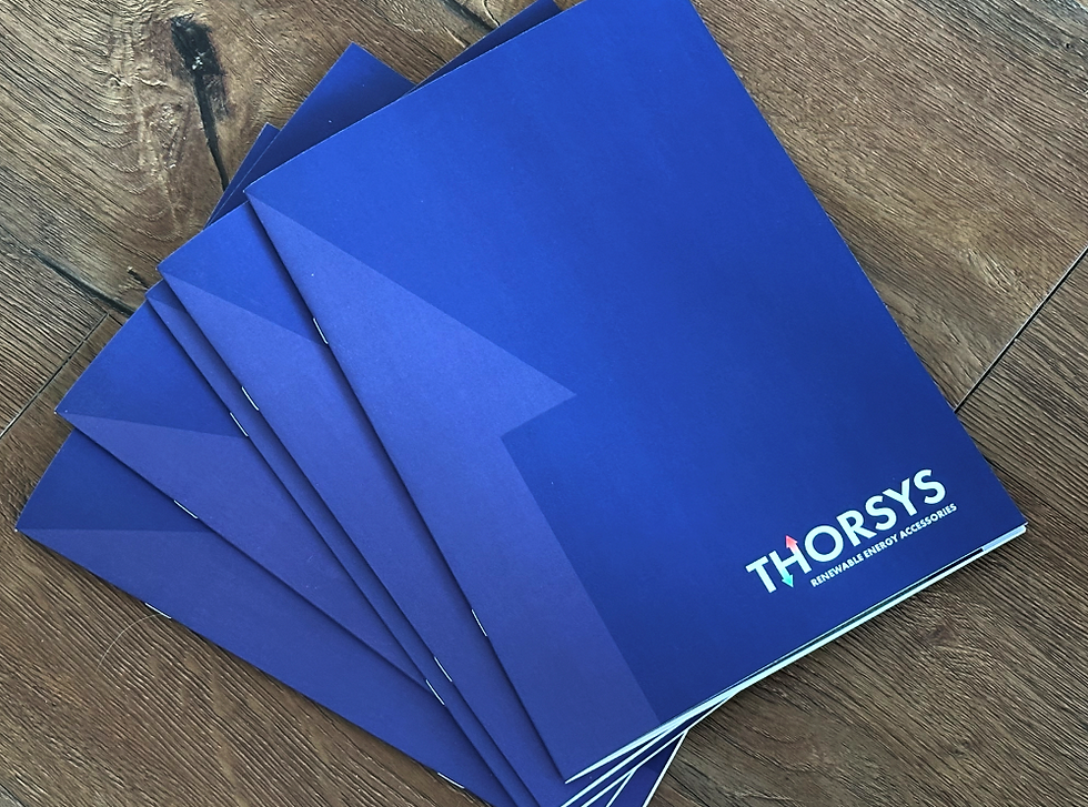 Blue folders with the "THORSYS" logo are fanned on a wooden surface. Each folder has a blue arrow design and text: "RENEWABLE ENERGY ACCESSORIES."