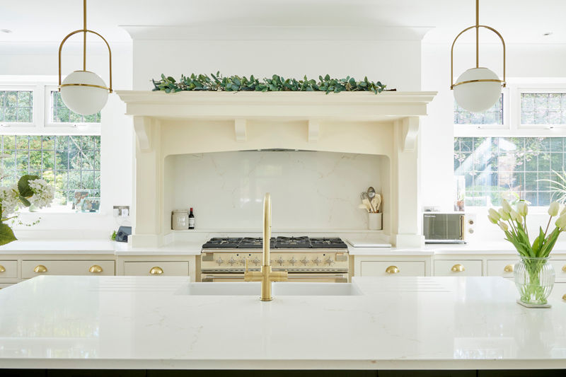 Bright kitchen with a marble island, gold faucet, range stove, white cabinets, and overhead greenery. Tulips and globe lights add elegance.