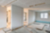 Unfinished room under renovation with white partition walls, exposed wiring, a window, and construction materials on the floor.