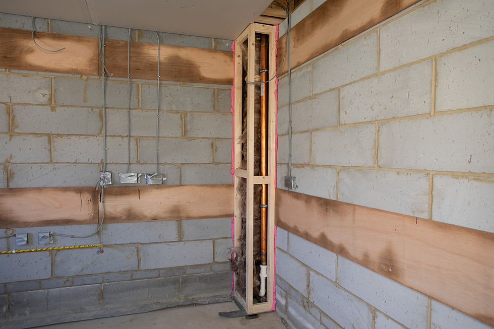Unfinished room with exposed brick walls, metal pipes, and insulation visible in a corner. Electrical wires hang from the ceiling.