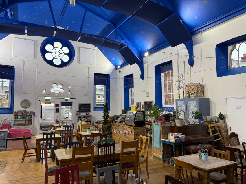 Bright cafe with blue arched ceiling, wooden tables and chairs, counter display, and large flower window in a cozy, empty room.