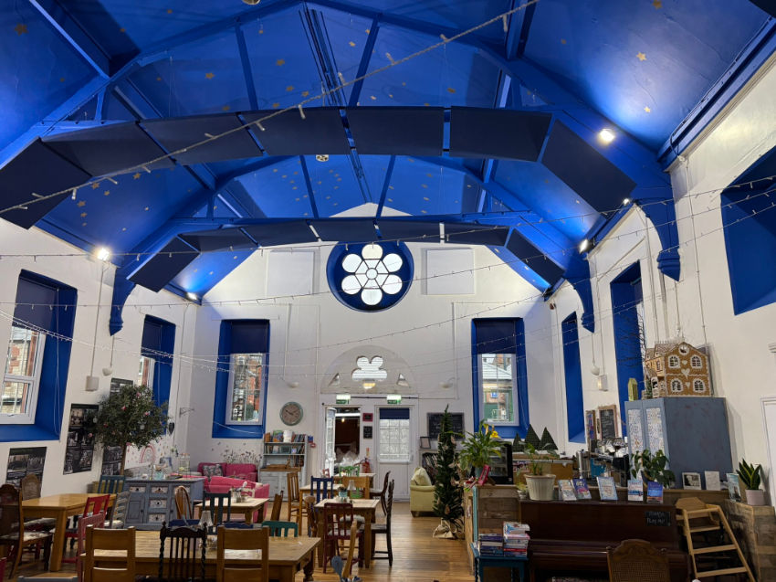 Bright café interior with blue vaulted ceiling, round window, wooden tables and chairs, plants, and cozy decor in a lively space