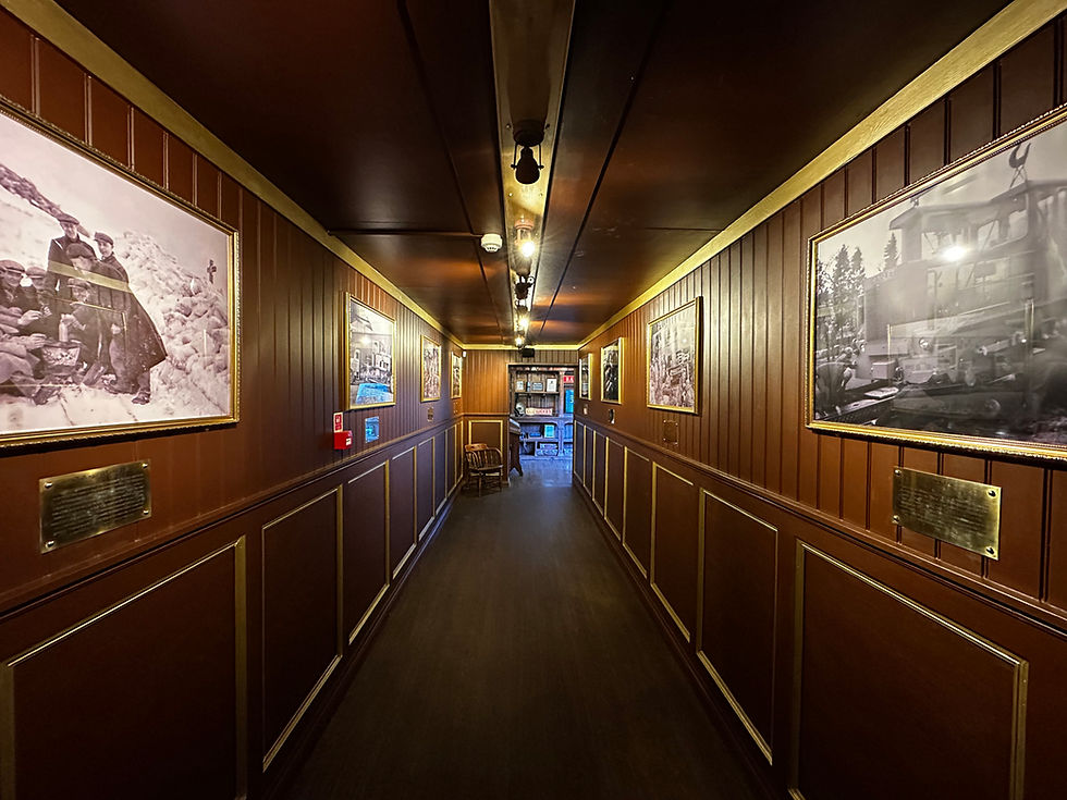 Wood-paneled hallway with framed historical photos on walls, dim lighting, leading to a blue-lit area. Mood is nostalgic and warm.