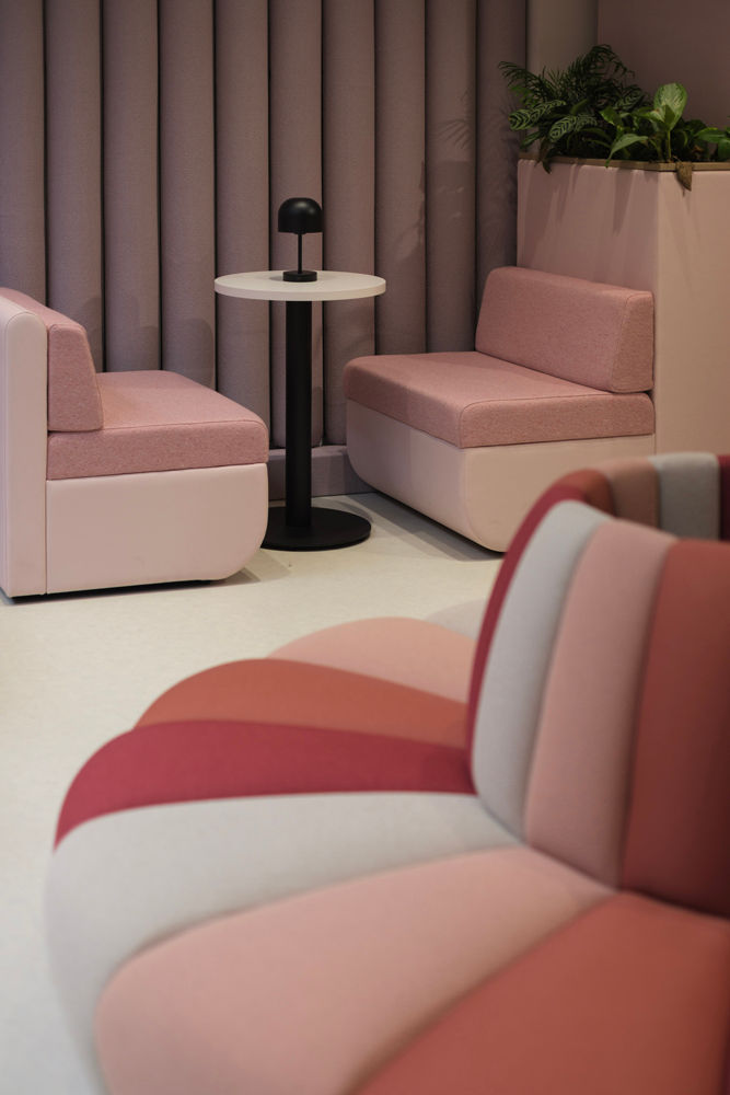 Pink and red seating with a round white table, black lamp, and plants in a cozy room. Walls have pink, cylindrical panels.