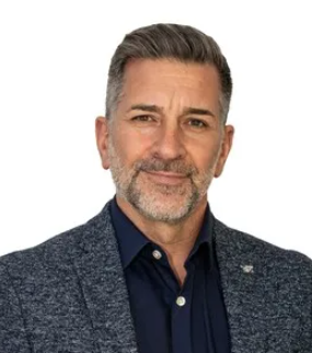 Middle-aged man with salt-and-pepper hair in a blue blazer and shirt, smiling softly against a white background.