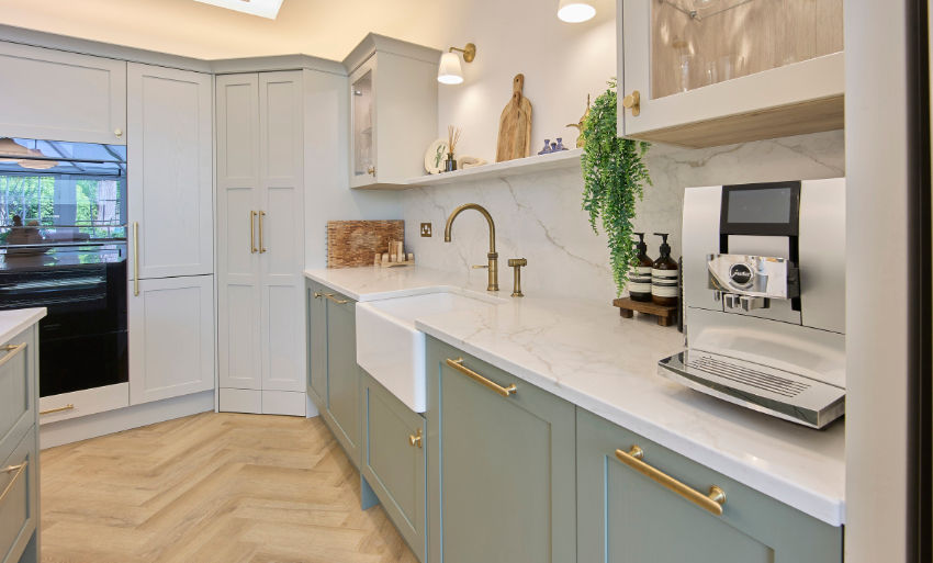 Bright modern kitchen with sage cabinets, marble counters, farmhouse sink, built-in coffee machine, and wood floor.