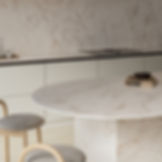 Modern marble kitchen with round table, two wooden chairs, and books labeled FRANK and MAEKAWA II on a calm neutral backdrop