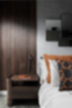 Modern bedroom with wood panel wall, brown nightstand, and pillows in brown and black patterns. A notebook and pen on the table. Calm mood.