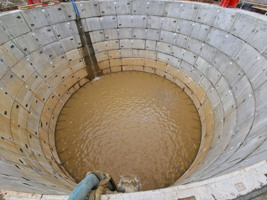 Top view of a large circular concrete pit filled with muddy water, with a blue hose draining water at the edge.